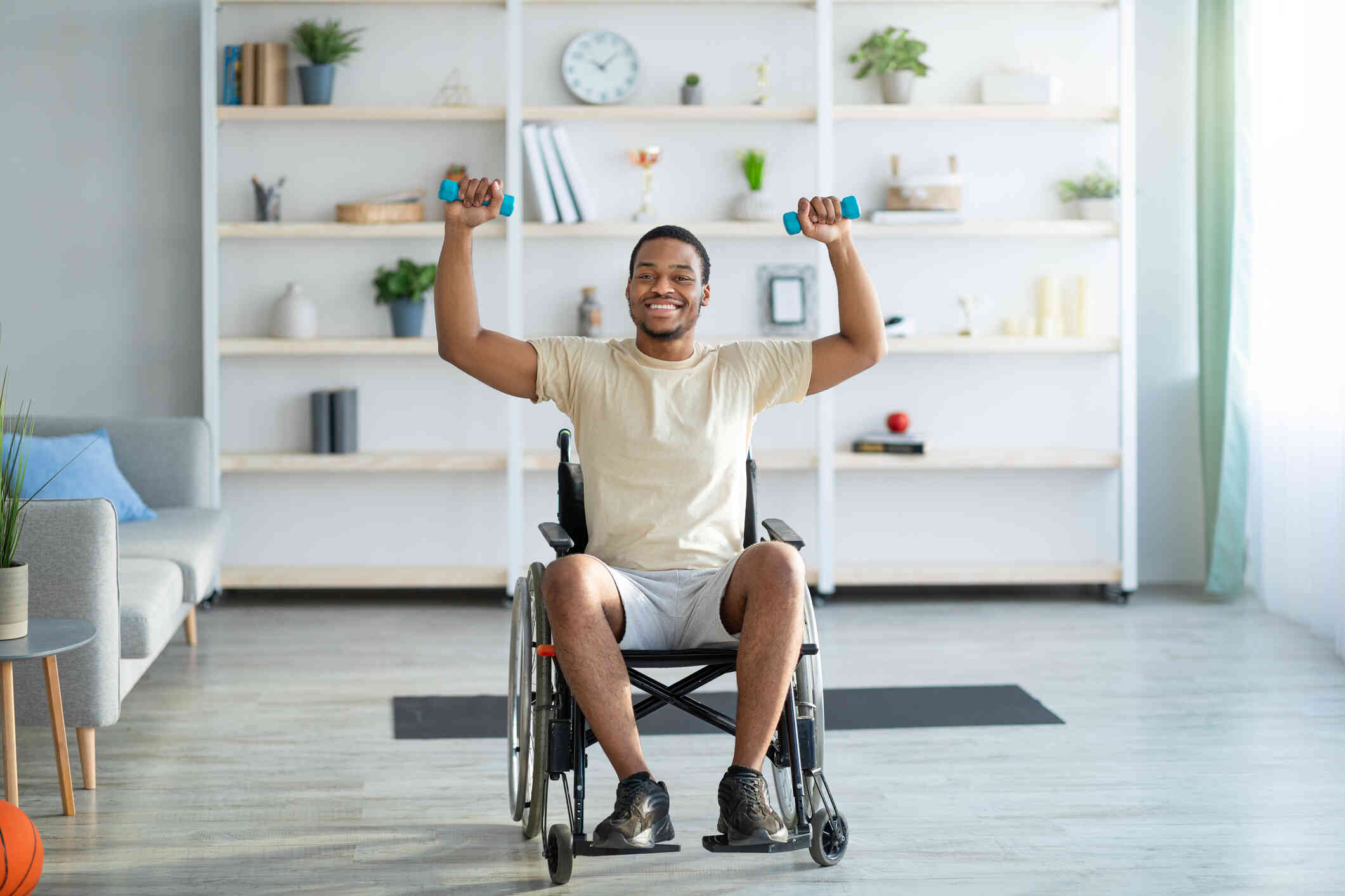 A man in a wheelchair exercises with dumbells while smiling and looking at the camera.